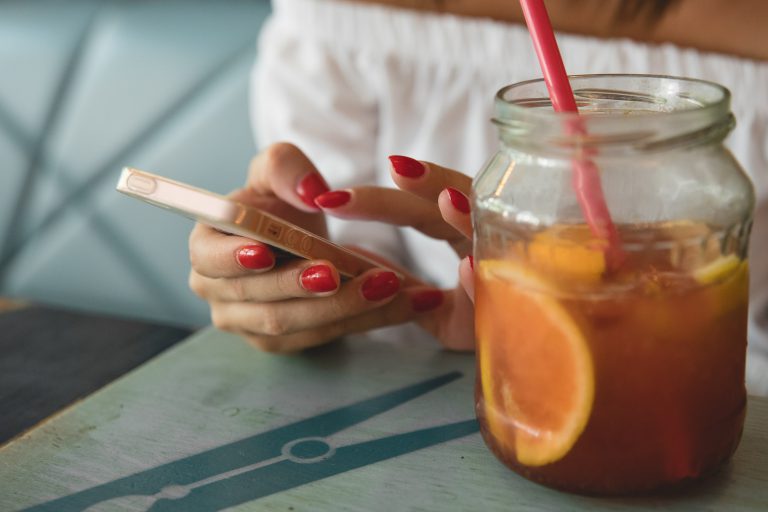 woman with red nail polish using phone