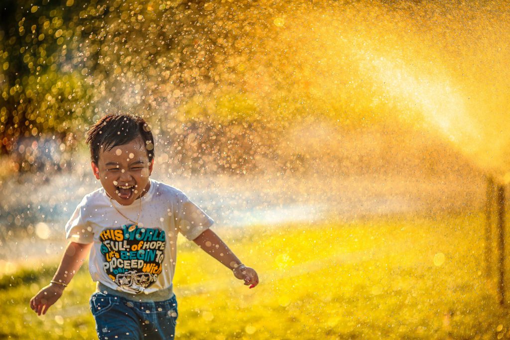 little boy playing and laughing, in splash of water, sunset