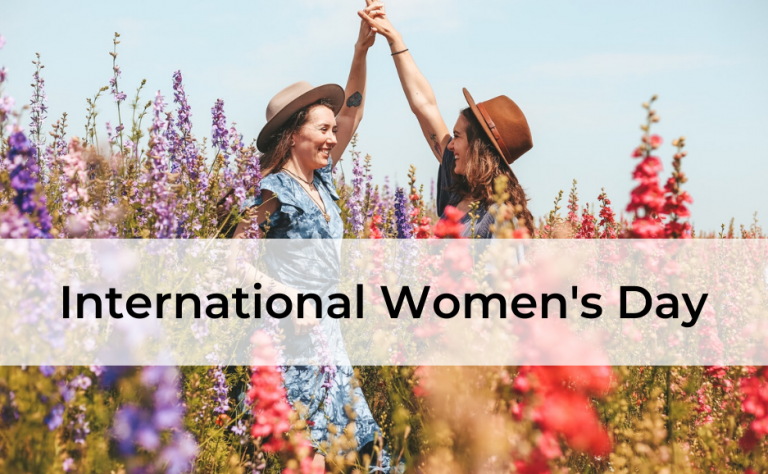 International Women's Day, two women in flower field holding hands and smiling